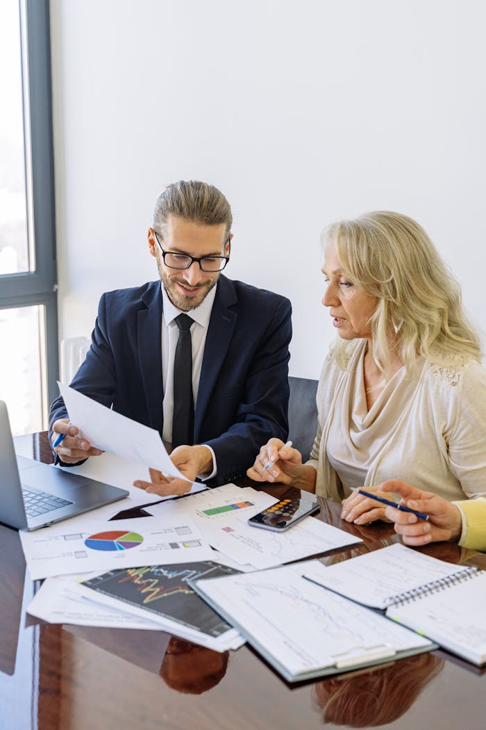 Two business professionals reviewing financial documents and graphs during a meeting.